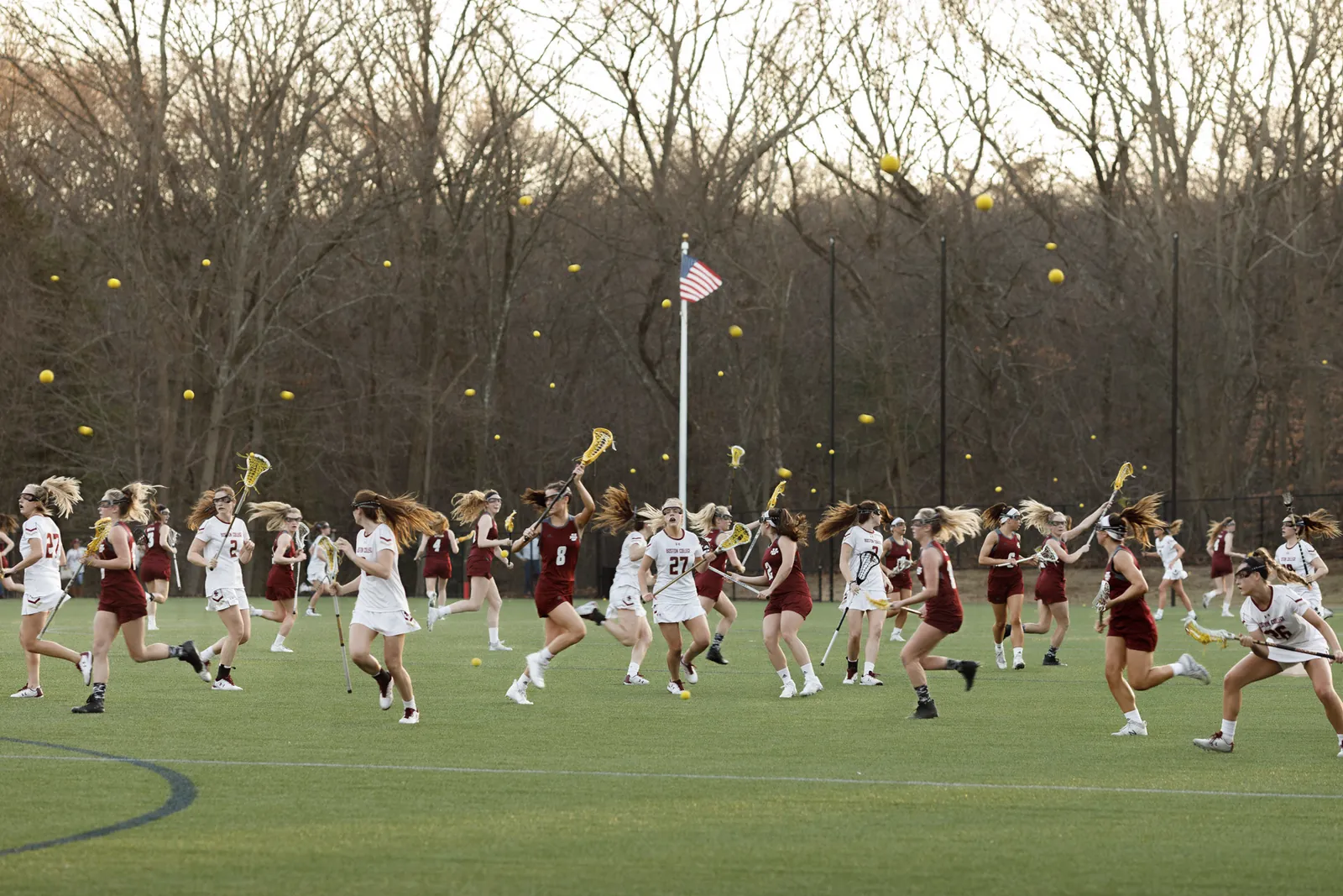 A lacrosse field crowded with overlapping players as dozens of yellow balls hang in the air
