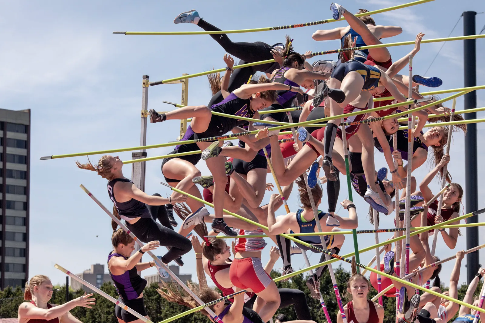 Dozens of pole vaulters overlaid mid-flight above a thicket of crossing poles