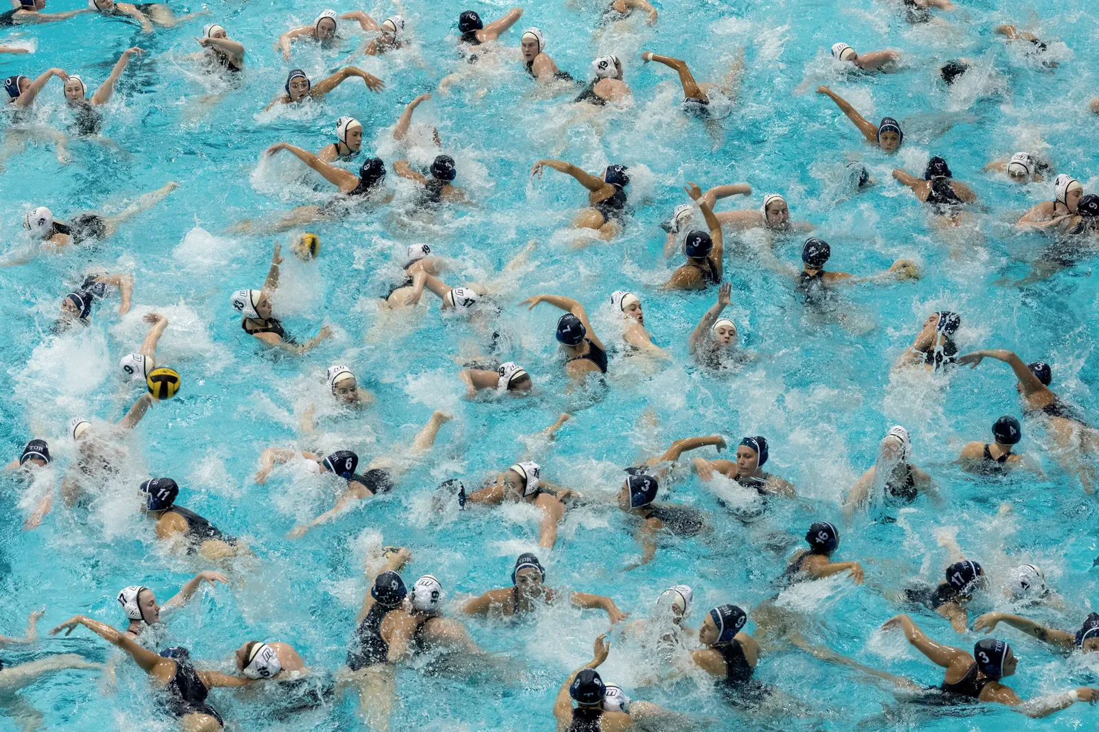 A pool seen from above, dense with overlapping water polo players mid-stroke